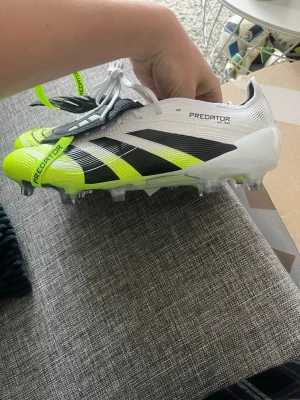Adidas Predator fotbollsskor vit/gul - Säljer ett par Adidas Predator fotbollsskor i vitt med neon-gula och svarta detaljer. Skorna är helt oanvända med alla lappar kvar. Skorna är i strl 42 och säljs för att dom e för små. Nypris är cirka 3000. Vid frågor är det bara att höra av sig.