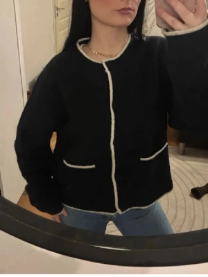 Supermysig alpacka kofta💕 - Mysig svart Alpacka/ull  kofta med vita kontrastkanter och rund hals. Koftan har knappar framtill och två fickor med vit kant. Modellen är loose fit och har långärmade ärmar. Materialet är stickat och känns fluffigt och mjukt. Strl L men passar perfekt på mig som är xs/s-m ❤️