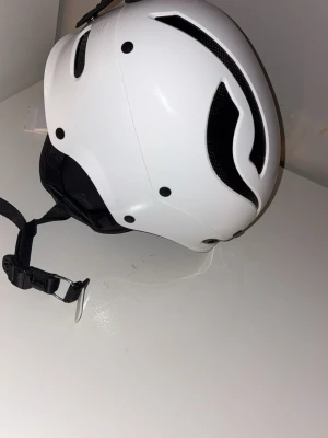 Vit Sweet protection skidhjälm med MIPS-system - Snygg vit hjälm med svart ventilationsdesign och MIPS-system för extra säkerhet. Justerbart hakband och vadderade öronpartier för skön passform. Perfekt för vintersport eller cykling. Modern look och lätt material.