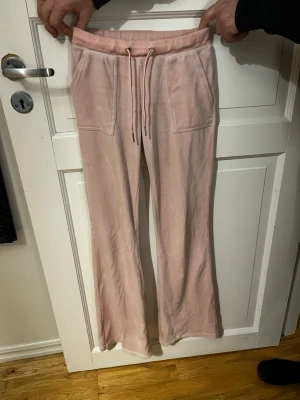 Ljusrosa mjukisbyxor med fickor - Säljer ett par ljusrosa mjukisbyxor med bred resår i midjan och dragsko. Byxorna har två stora framfickor och två bakfickor med lock och knappdetaljer. Materialet är mjukt och skönt, perfekt för chill dagar. Raka ben och avslappnad passform.