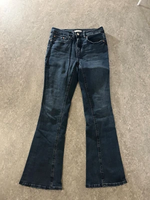 Mörkblå bootcut jeans - Snygga mörkblå bootcut jeans med klassisk femficksmodell och kontrastsömmar. Jeansen har normal midja och utsvängda ben, perfekta för en trendig och avslappnad look. Tillverkade i mjukt denimtyg som ger en skön känsla hela dagen.
