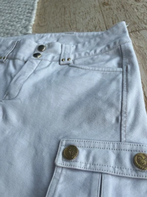 Vita tävlingsbyxor från Hööks - Snygga vita tävlingsleggins från Hööks Collection med dubbla silverknappar i midjan och dekorativa guldknappar på fickorna. Byxornas material är bekvämt och de har klassiska fickor framtill. Perfekt för dig som gillar stilrena detaljer.