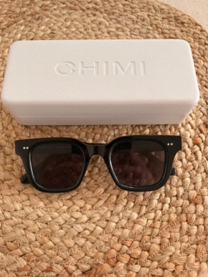 Svarta solglasögon från CHIMI 04 - Snygga svarta solglasögon från CHIMI 04 med klassisk rektangulär form. Glasögonen har svarta bågar i syntetmaterial och mörka linser. Perfekta för att lyfta din stil under soliga dagar.