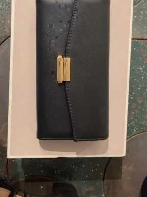 Svart kuvertväska från Anna Field - Snygg svart kuvertväska från Anna Field i läder med guldfärgat spänne framtill. Väskan har flera fack, inklusive dragkedjefack och plats för kort. Har endast använt den en gång på balen och jag fick plats med allt jag behövde som kort telefon och lite andra småsaker. Den är 15cm bred och 7cm hög:)