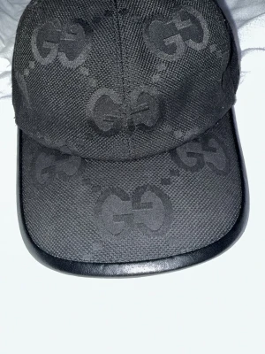 Svart keps från Gucci med GG-mönster - Snygg svart keps från Gucci med det klassiska GG-monogrammet över hela kepsen. Kepsen har böjd skärm med läderkant och justerbart spänne bak. Tillverkad i slitstarkt tyg som ger en exklusiv känsla och passar perfekt till streetwear-stilen. Tar gärna emot byten de vita i kepsen är hårsprej för jag formade den