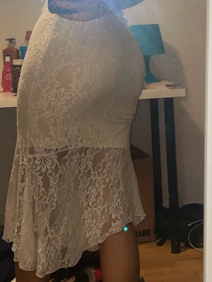 Vit spetskjol med blommigt mönster!  - Säljer en lång, vit kjol i spets med blommigt mönster. Kjolen har en figurnära passform upptill och volang nedtill, vilket ger en snygg siluett. Perfekt för dig som vill ha en romantisk och trendig look.