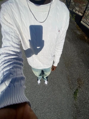 Vit kabelstickad tröja från GANT - Vit kabelstickad tröja från GANT med rund halsringning och diskret logga på bröstet. Tröjan har en klassisk passform och är tillverkad i mjuk bomull. Perfekt för lager-på-lager och funkar året runt.