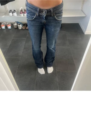 Vintage bootcut jeans - Säljer ett par snygga blå jeans från Lee med låg midja och bootcut-ben. Jeansen har slitna detaljer, dubbla knappar i midjan och klassiska fickor fram och bak. Storlek W27 L31, skriv för frågor och prisförslag. Kan gå ner i pris!💗