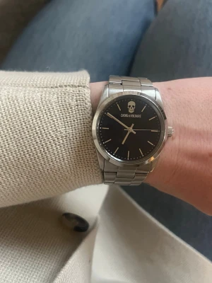 Zadig & Voltaire silverklocka - Stilren klocka från Zadig & Voltaire med mörkblå urtavla, silverfärgade visare och index samt en ikonisk döskalle upptill. Armbandet är i blankt silverfärgat metall och ger en clean look. Perfekt accessoar för dig som gillar edgy detaljer.