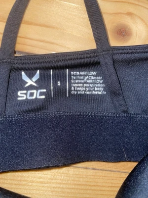 Svart sport-bh från SOC - Sport-bh från SOC i svart funktionsmaterial med tunna axelband och korsad rygg. Materialet har TCS Airflow-teknologi som transporterar bort svett och håller dig torr och bekväm under träningen. Perfekt för gym, löpning eller yoga. Sparsamt använd.