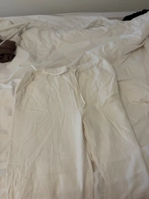 Vita linnebyxor från Pull&Bear - Säljer ett par vita linnebyxor från Pull&Bear med avslappnad passform och resår i midjan. Byxorna har dragsko och sidofickor, perfekta för en chill och stilren look. Materialet är svalt och luftigt linne, vilket gör dem riktigt sköna att bära.