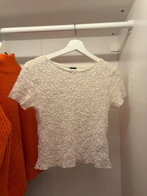 Vit spetsblus från Gina Tricot - Säljer en söt vit blus från Gina Tricot i storlek M. Toppen har korta ärmar och är helt täckt av spets med ett krinklat, stretchigt tyg. Perfekt att styla med jeans eller kjol för en trendig look.