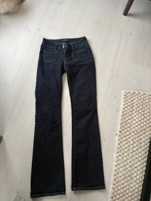 Mörkblå bootcut jeans med fickor från madlady  - Säljer ett par mörkblå bootcut jeans med två stora framfickor och markerade sömmar. Jeansen har hög midja och klassisk knappgylf. Perfekta för dig som gillar en retroinspirerad look och vill ha ett par jeans som sticker ut lite extra.Jag är cirka 172 cm men kan också sys upp. 