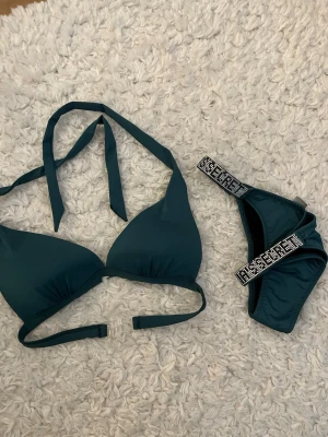 Mörkgrön bikini Victoria's Secret - Supersnygg mörkgrön bikini från Victoria's Secret med vadderad trekants-bh och knyt i nacken. Bikinitrosan har breda band med glittriga detaljer i silver. Perfekt för sommarens strandhäng!