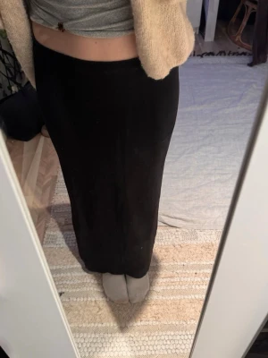 Svart långkjol i bomull - En enkel och stilren svart långkjol i mjukt bomullsmaterial. Kjolen har en rak passform och är perfekt för dig som gillar minimalistisk stil. Passar till många olika outfits och är lätt att matcha med både toppar och tröjor.