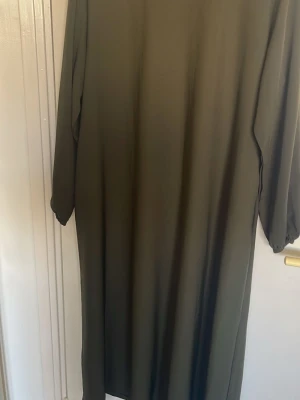 Mörkgrön långklänning med långa ärmar - En enkel och stilren mörkgrön långklänning med långa ärmar. Klänningen har rak passform och är tillverkad i ett mjukt, lätt material som faller snyggt. Perfekt för dig som gillar minimalistisk stil.