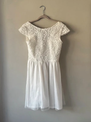 Studentklänning/Vit klänning  - Säljer en jättefin vit klänning med spetsdetaljer upptill och en lätt, luftig underkjol. Stängs bak med dragkedja samt fina knappar.  Storlek 38/M  Perfekt till sommarfest, skolavslutning eller student! Köptes 2021, verkar inte finnas att köpa helt ny längre.   Prislapp kvar så aldrig använd! Valde att behålla en annan storlek. Jag är 1,57 och en storlek större på mig gick till knäna. Om önskemål finns kan jag mäta längden på klänningen. 