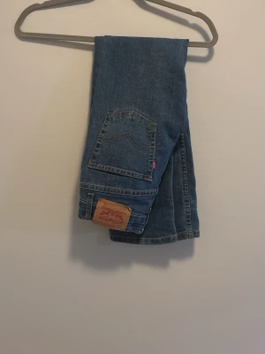 Blå Levi's jeans med klassisk passform - Säljer ett par blå Levi's jeans med klassisk femficksdesign och rak passform. Jeansen har den ikoniska läderpatchen bak och röd Levi's-tag på bakfickan. Materialet är slitstark denim i bomull och färgen är mediumblå.
