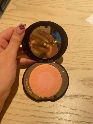 Charlotte Tilbury puder blush duo - Säljer ett puderrouge från Charlotte Tilbury i en snygg persikoton med en ljusare rosa mitt. Kommer i en rund, mörkbrun plastdos med spegel i locket och guldig detalj på utsidan. Perfekt för att ge kinderna ett fräscht glow. Färg: Love Glow. Nypris: 570 kr.