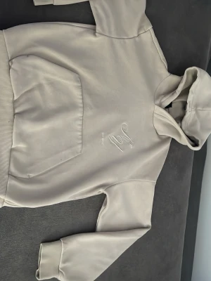 Beige hoodie från 19V69 Italia - Snygg beige hoodie från H&M med broderad logga på bröstet. Klassisk känguruficka framtill och ribbade muddar vid ärmar och nederkant. Tillverkad i mjukt material som känns skönt mot huden. Perfekt för en avslappnad och trendig look.