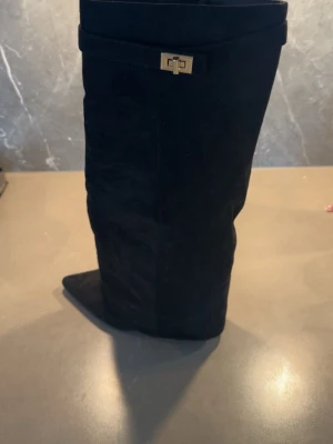 Svarta höga mockastövlar med klack - Snygga svarta stövlar i mocka med spetsig tå och bred klack. Dekorativt spänne i guld upptill! 