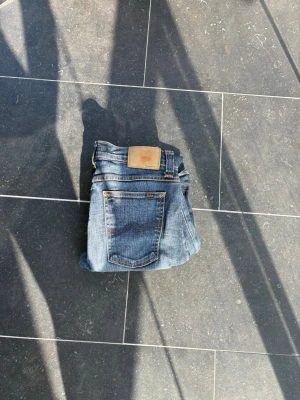 Blå slim fit jeans från nudie  - Snygga blå slim fit jeans från nudie med klassisk femficksdesign och läderpatch bak i midjan. Jeansen har en lätt tvättad look och smala ben, perfekta till sneakers eller boots. W28 L34