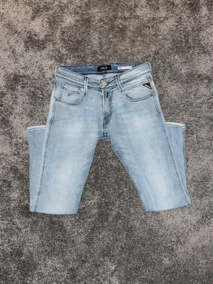 Ljusblå Replay Anbass - Snygga ljusblå jeans från Replay med klassisk femficksdesign och slim-fitt passform. Jeansen har tydliga kontrastsömmar och en liten logotypdetalj på fickan fram. Tillverkade i mjukt denimtyg som ger en avslappnad look.