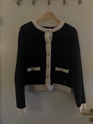 Svart kofta med vita detaljer - Stilren svart kofta med vita kanter och guldknappar framtill. Koftan har två små fickor med vita detaljer och är långärmad. Perfekt för en trendig och klassisk look.Hör av dig om du har några frågor! 💗🫶🏼