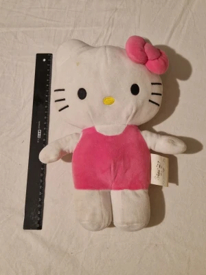 Hello Kitty mjukisdjur - Söt Hello Kitty mjukisdjur i vitt och rosa plysch med en rosa klänning och matchande rosett på huvudet. Ansiktet har broderade detaljer och figuren är ca 30 cm lång.