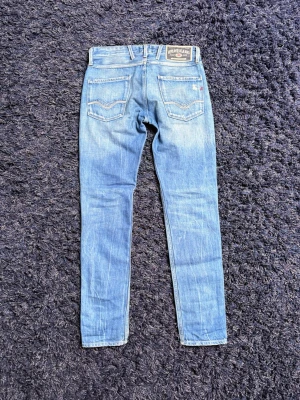 Replay jeans - Säljer ett par ljusblå jeans från Replay med slitningar på knäna och klassiska fem fickor. Jeansen har en snygg tvättad look med snygg bakficka. Perfekta för en avslappnad och trendig stil. Hör av er vid minsta fundering!