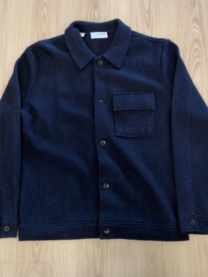 Mörkblå overshirt från Selected Homme - Stilren mörkblå overshirt från Selected Homme i ullmix. Klassisk rak passform med krage, knappstängning framtill och en bröstficka med lock. Perfekt lager-på-lager-plagg för en clean och modern look.