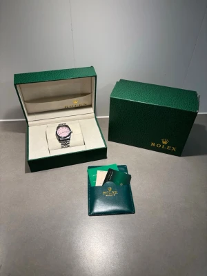 klocka med rosa urtavla - Snygg klocka i rostfritt stål med jubilee-länk och en unik rosa urtavla med diamanter som timmarkeringar. Klockan levereras i original grön med certifikat och tillbehör. Perfekt accessoar för dig som vill sticka ut med stil.