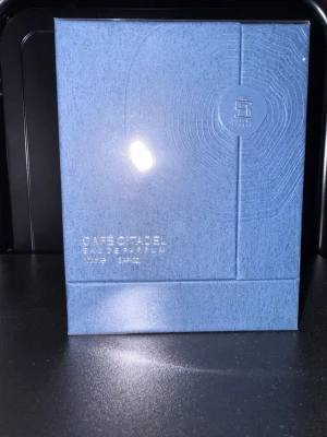Café Citadel Eau de Parfum blå - Café Citadel Eau de Parfum från Aurora Scents i en snygg blå förpackning med stilren design. Parfymen kommer i en rektangulär box med silverdetaljer och subtila mönster. Perfekt för dig som gillar exklusiva dofter.