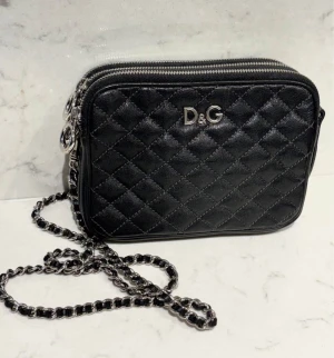 Dolce Gabbana vintage perfekt skick - Quiltad svart skinn väska från D&G med silverfärgad detaljer. Väskan har tre fack med dragkedja och perfekt som festväska eller snygg vardagsväska.  Perfekt för dig som gillar lyxiga accessoarer.