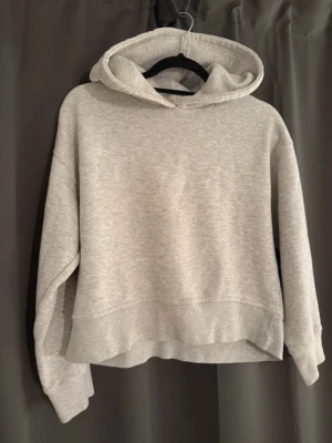 Ljusgrå hoodie med huva - En stilren ljusgrå hoodie i mjukt material med avslappnad passform och klassisk huva. Perfekt för en chill och bekväm look. Hoodien har långa ärmar och ribbade muddar vid ärmslut och nederkant.