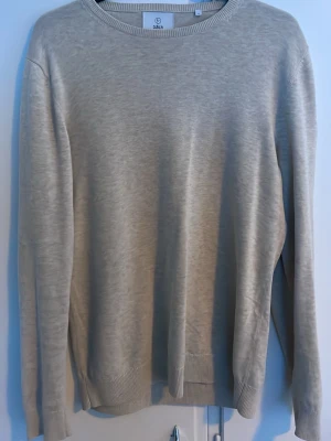 Ljusgrå stickad tröja från Bläck - En stilren ljusgrå stickad tröja från Bläck med rund halsringning och ribbade muddar vid ärmslut och nederkant. Tröjan har en enkel och klassisk design som passar till det mesta. Perfekt för lager på lager och enkel att matcha.