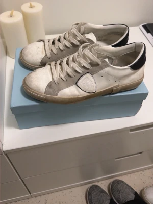 Philippe Model skor - Priset är ej hugget i sten, väldigt bra skick! vita sneakers från Philippe Model med gråa och svarta detaljer. Skorna har en klassisk låg siluett, vita skosnören och en beige sula. Tillverkade i en mix av läder och mocka för en cool och avslappnad look.