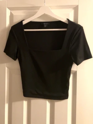 Svart croppad topp - Svart croppad topp med fyrkantig halsringning och korta ärmar. Toppens material är slätt och har en tight passform. Passar till de flesta plagg i garderoben. 