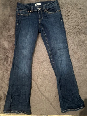 Mörkblå bootcut jeans från Gina - Säljer ett par mörkblå bootcut  jeans från Lee med klassiska kontrastsömmar och femficksmodell. Jeansen har knapp- och dragkedjegylf samt bakfickor med lock och knapp. Tillverkade i slitstark denim med snygg tvätt