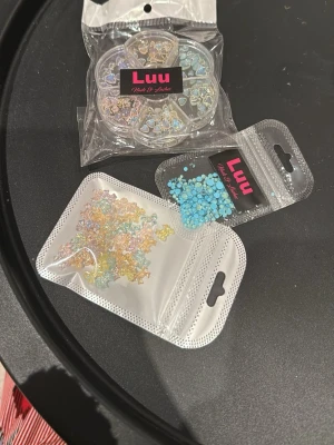 Nageldekorationer - Säljer flera förpackningar nageldekorationer. Innehåller små pärlor och blommor i blått, gult och iriserande färger. Perfekt för att skapa unika och kreativa nageldesigner. Kommer i praktiska förpackningar och hjul för enkel användning.