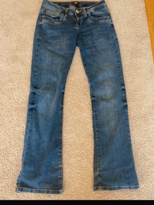 Blå bootcut jeans från LTB - Snygga blå bootcut jeans från LTB med klassisk femficksmodell och låg midja. Jeansen har slitningar och kontrastsömmar för en trendig look. Tillverkade i mjuk denim med lite stretch för extra komfort.