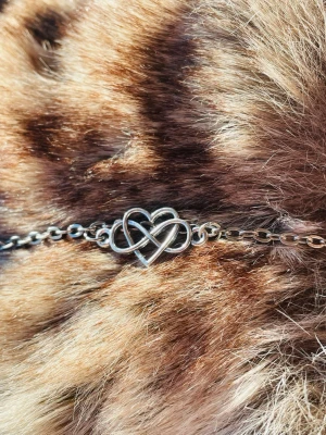 By prisförslag- Silverfärgat halsband katt/liten hund med hjärtdetalj - Snyggt halsband i silverfärgad metall med en detalj i form av två sammanflätade hjärtan. Passar katter eller en liten hund. Kedjan är tunn och stilren, perfekt för dig som gillar minimalistiska smycken med en romantisk touch. 