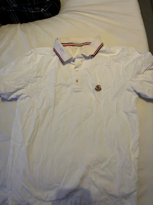 Vit pikétröja från Moncler - Vit pikétröja från Moncler med klassisk krage och knäppning framtill. Tröjan har Moncler-logga på bröstet