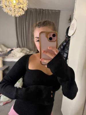 Svart stickad sweetheart-tröja - Svart stickad tröja med sweetheart-urringning och långa ärmar. Tröjan är ribbstickad och har en figurnära passform som framhäver siluetten. Perfekt för att skapa en trendig look.