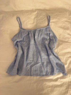 Söt linnetopp från H&M - Säljer en fräsch och luftig linnetopp från H&M i storlek M. Toppen har tunna axelband och är vit med smala blå ränder. Materialet är mjukt och känns som bomull, perfekt för varma dagar. Enkel och stilren design som är lätt att matcha med jeans eller shorts.