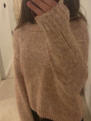 Beige/rosa stickad tröja - Mysig stickad tröja i beige med inslag av ljusa toner. Tröjan har en lös passform, bred ribbad mudd vid ärmslut och nederkant samt rund halsringning. Perfekt för lager på lager och en avslappnad stil.