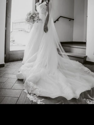 fantastiska italienska bröllopsklänning från 2025 – en riktig showstopper  - Klänningen har en elegant, den glittrande tyllen tillsammans med handsydda spetsapplikationer ger ett mjukt, romantiskt fall som skimrar vackert i både sol och kvällsljus. Den långa släpet ger en kunglig känsla utan att bli tung. Perfekt för sommarbröllop – både utomhus och i kyrka.  Exklusiv italiensk design Lätt och luftig – perfekt för sommar 2025 Storlek 36–38–40 