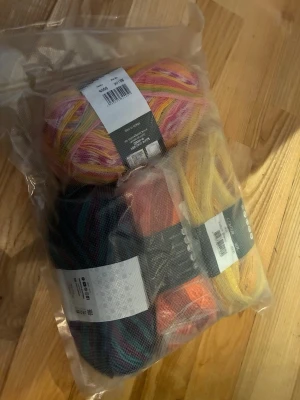 Flerfärgat garnpaket Scheepjes - Säljer ett paket med fyra nystan garn från Scheepjes i olika färger: gul, orange, rosa, blå, lila och flerfärgat. Perfekt för stickning eller virkning. Garnet är packat i en genomskinlig plastpåse och innehåller både Colour Crafter och andra varianter.