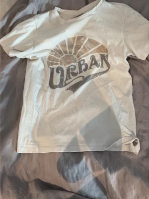Vit t-shirt med Urban-tryck - Snygg vit t-shirt med ett stort tryck där det står Urban. Klassisk rund halsringning och korta ärmar. Den är från Vila i storlek M