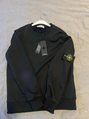 Svart sweatshirt från Stone Island - Säljer en svart sweatshirt från Stone Island med den ikoniska patchen på ärmen. Tröjan har rund hals, ribbade muddar och är tillverkad i mjuk bomull. Perfekt för dig som vill ha en clean och stilren look med streetwear-vibe. Använt fåtal gånger. Pris går att diskutera. För mer bilder eller frågor de e ba att skriva 